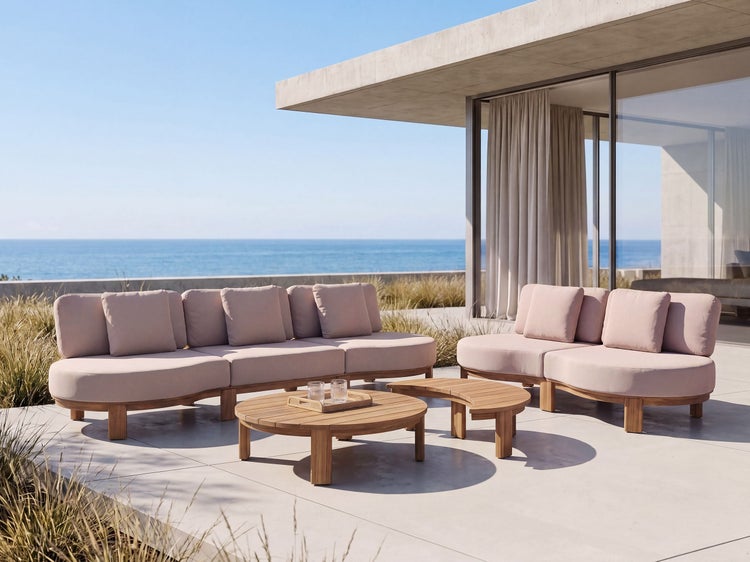 Moderne Lounge-Gartenmöbel mit weichen Polstern und runden Holztischen auf einer Terrasse mit Meerblick.