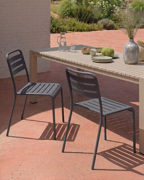 Moderne Außensitzgruppe mit zwei dunkelgrauen Metallstühlen und einem hellen Lamellentisch auf einer sonnigen Terrasse im schlichten Design.