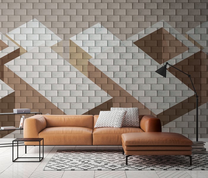 Moderner Wohnraum mit geometrischer Fototapete in Backsteinoptik, cognacfarbenem Ledersofa, passendem Hocker, schwarzer Stehleuchte und Teppich.
