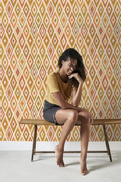 Frau sitzt vor einer Wand mit Rautenmuster-Tapete auf einer Holzbank