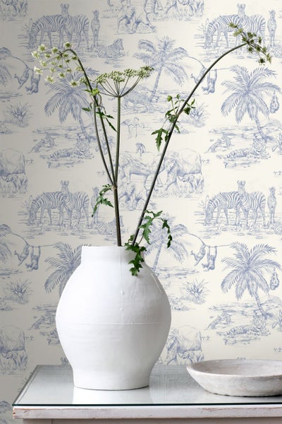 Vliestapete mit Safari-Motiven im Toile-de-Jouy-Stil mit Elefanten, Zebras und Palmen in Blau auf hellem Hintergrund.