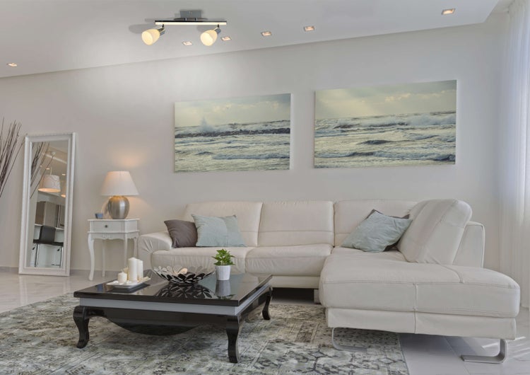 Helles Wohnzimmer mit Sofa, Couchtisch, Bildern und Deckenleuchten.