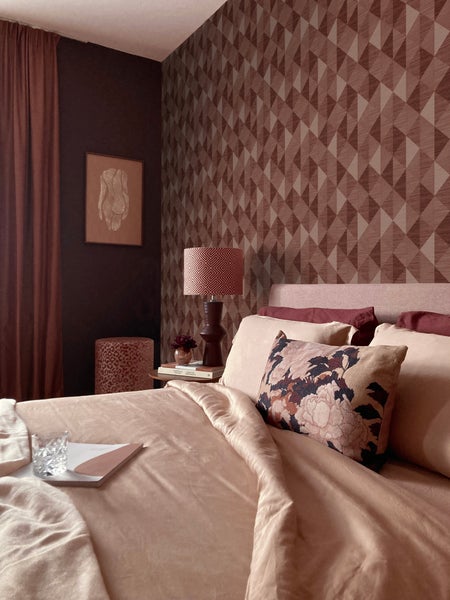 Ein Schlafzimmer mit einem Bett, einer Lampe und einer geometrischen Tapete