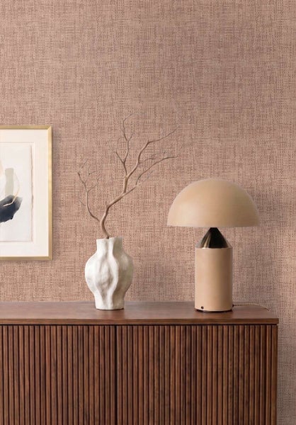 Wohnzimmer mit Vliestapete in Textiloptik, dazu ein geriffeltes Sideboard aus Holz, eine moderne Tischleuchte und eine abstrakte Wanddekoration.