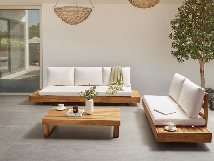 Moderne Garten-Lounge-Gruppe aus hellem Holz mit weißen Polstern, bestehend aus Dreisitzer, Zweisitzer und Couchtisch auf einer grauen Terrasse.