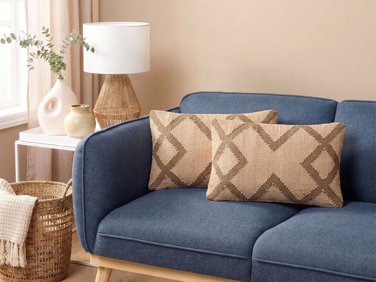 Zwei dekorative Kissen mit geometrischem Muster auf einem blauen Sofa in einem wohnlich eingerichteten Raum mit Lampe und Korb.
