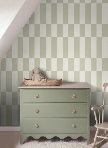 Kinderzimmer mit karierter Tapete, einer grünen Holzkommode mit drei Schubladen und einem geflochtenen Korb mit Kuschelhasen.