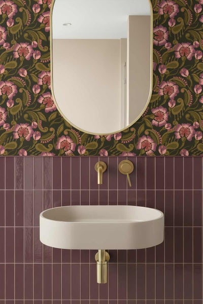 Modernes Badezimmer mit floral gemusterter Tapete, bordeauxroten vertikalen Fliesen, ovalem Wandwaschbecken, goldenen Armaturen und ovalem Spiegel.