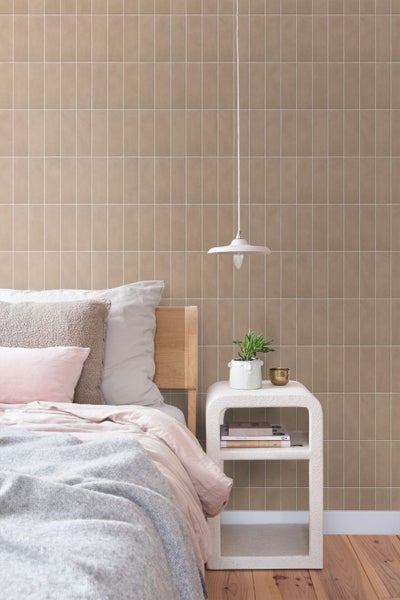 Schlafzimmer mit beigefarbenen Wandfliesen in Kacheloptik, Holzbett, modernem Nachttisch, Pendelleuchte und dekorativer Pflanze.