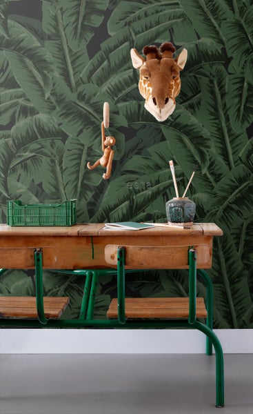 Vintage-Schreibtisch vor Wandtapete mit Dschungelmotiven, dekoriert mit Giraffenkopf, Spielzeugaffe und grüner Kiste.