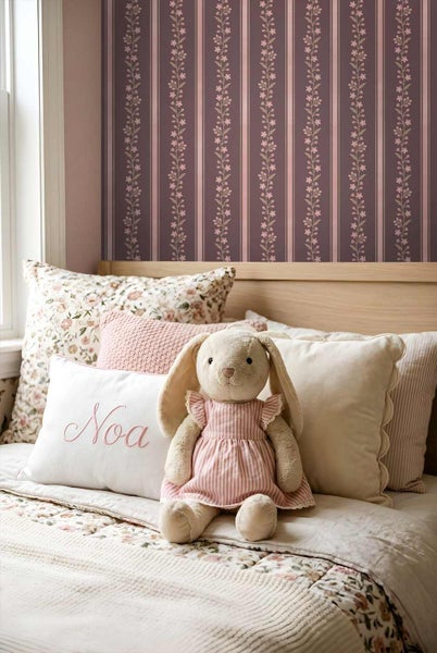 Kinderzimmer mit gestreifter Blumentapete an der Wand hinter einem Holzbett mit verschiedenen Kissen und einem Stoffhasen.