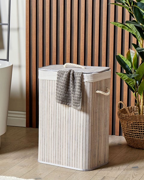 Rechteckiger Wäschekorb aus hellem Bambus mit Seilgriffen und grauem Handtuch in einem hellen Raum mit Holzlamellenwand.