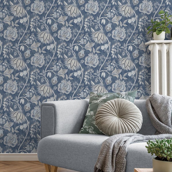 Wohnzimmer mit floral gemusterter Tapete, Sofa, Kissen und Zimmerpflanzen für eine gemütliche Atmosphäre.