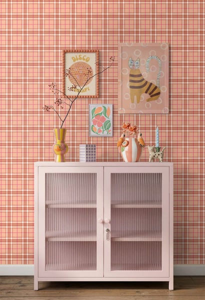 Vliestapete mit Karomuster hinter einer hellrosa Anrichte mit geriffelten Glastüren, dekoriert mit farbenfrohen Vasen und Wandbildern.