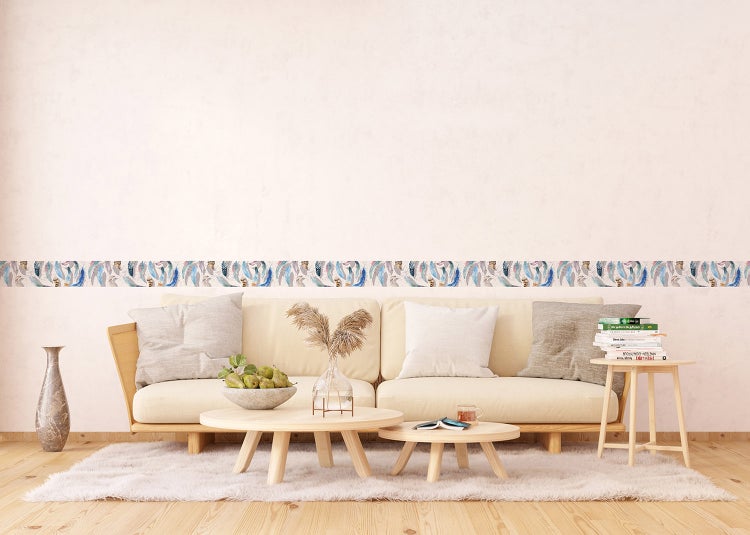 Selbstklebende Tapetenbordüre mit Federmuster in einem hellen Wohnzimmer über einem Sofa mit Holztischen und einem Teppich.