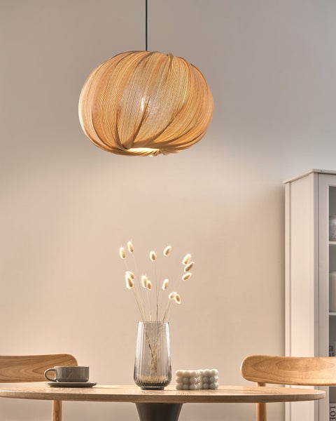 Runde Pendelleuchte mit Falten-Design über einem Esstisch aus Holz mit Blumenvase und Tasse in hellem, organisiertem Raum.