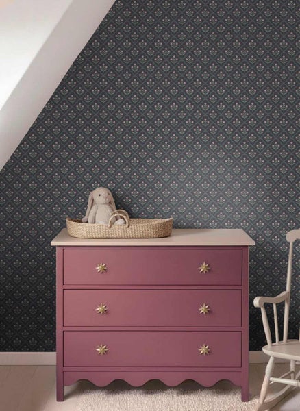 Dunkle Vliestapete mit kleinem floralem Muster in einem Kinderzimmer mit rosa Kommode und weißem Schaukelstuhl.