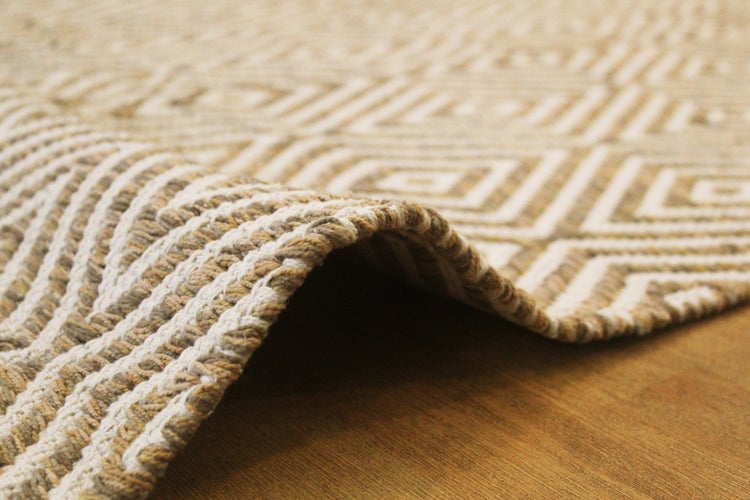 Gewebter Teppich in Beige und Weiß mit geometrischem Rautenmuster, Detailansicht der Textur und Kante.