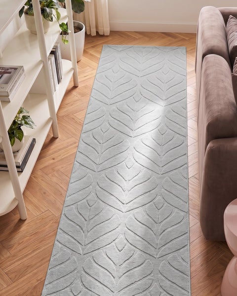 Teppichläufer mit Blattmuster auf Holzboden zwischen Regal und Sofa.
