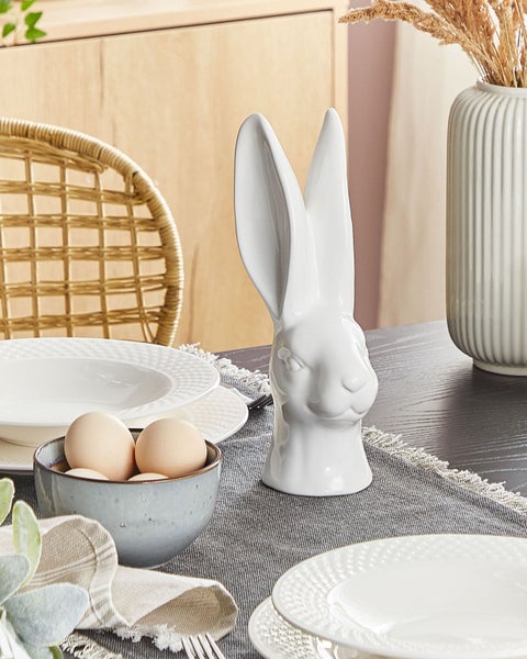 Dekorativer Ostertisch mit Porzellanhasen, Eiern, Geschirr und Tischdecke.