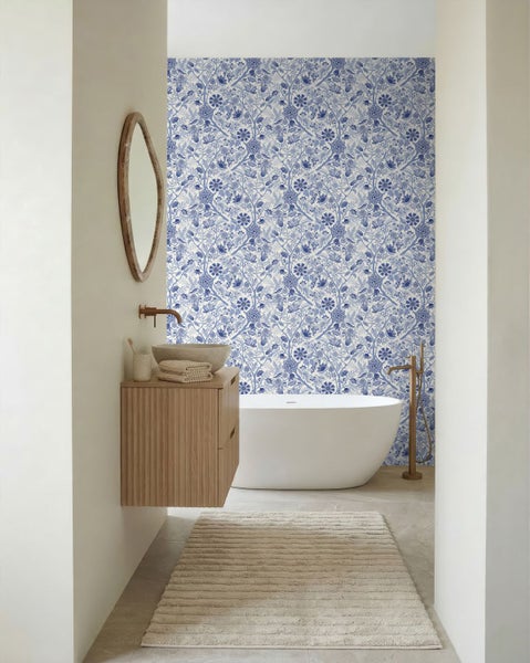 Helles Badezimmer mit blau-weiß geblümter Tapete, weißer freistehender Badewanne und Holzwaschtisch mit Steinbecken.