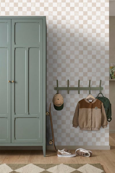 Kinderzimmer mit hellbeiger Schachbrett-Tapete, grünem Kleiderschrank, Hakenleiste mit Jacke und Kappe, Skateboard und Holzfußboden.
