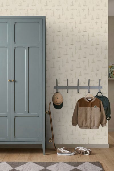 Kinderzimmer mit blauem Kleiderschrank, Segelschiff-Tapete, einer Garderobenleiste mit Kinderjacke und einem Skateboard auf Holzboden.