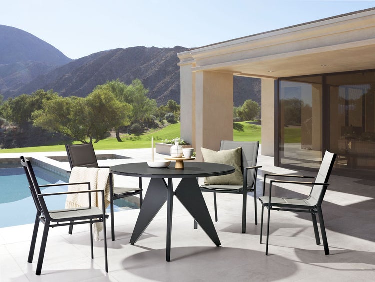 Gartenszene mit rundem Tisch und Stühlen auf einer Terrasse neben einem Pool mit Blick auf Berge