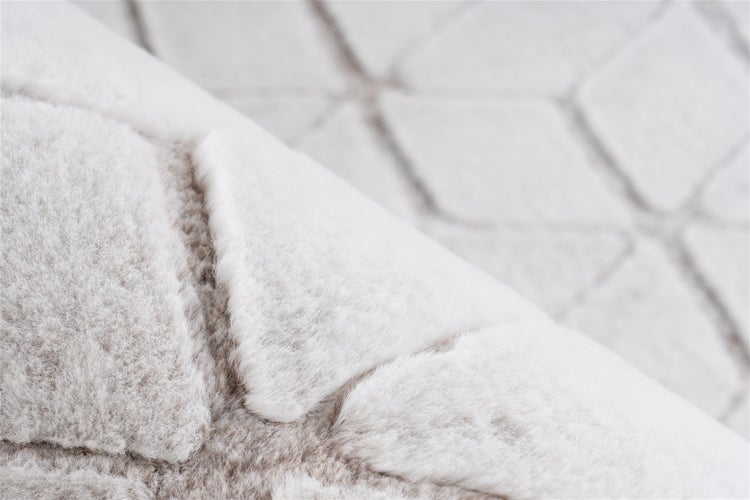 Nahaufnahme eines weichen Plüschteppichs mit geometrischem Muster und Hochflor-Textur.