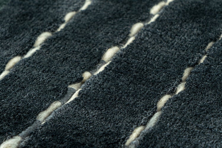 Nahaufnahme eines Hochflor-Teppichs mit strukturierter Oberfläche und dekorativen hellen Garnen.