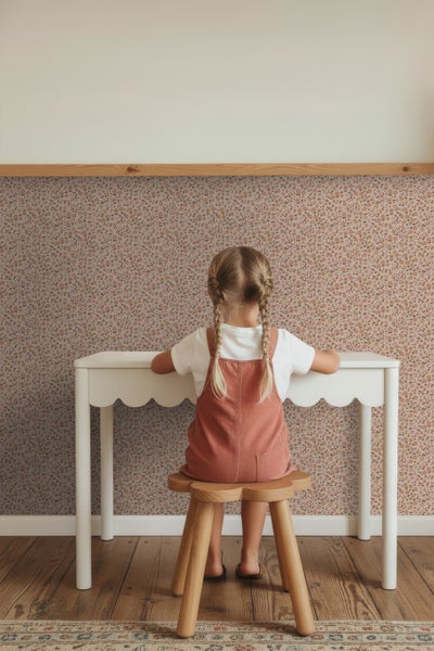 Mädchen sitzt an einem weißen Kindertisch vor einer floralen Tapete