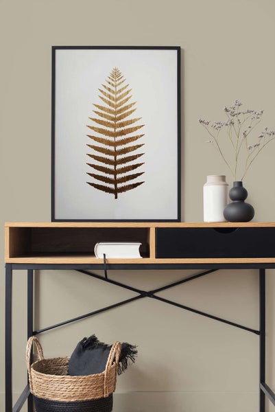 Gerahmtes Wandbild mit goldenem Farnblatt auf einem Schreibtisch aus Holz und Metall neben Vasen und einem Flechtkorb.