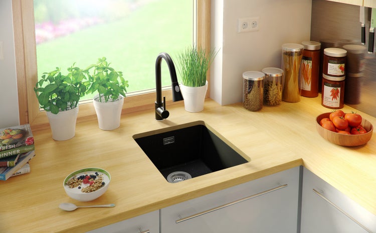 Küchenspüle mit Armatur auf einer Arbeitsplatte neben Lebensmitteln und Pflanzen