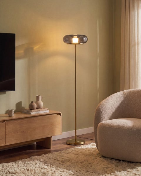 Moderne Stehleuchte mit gläsernem Schirm und filigranem Gestell in einem wohnlich eingerichteten Wohnzimmer mit TV und Sessel.