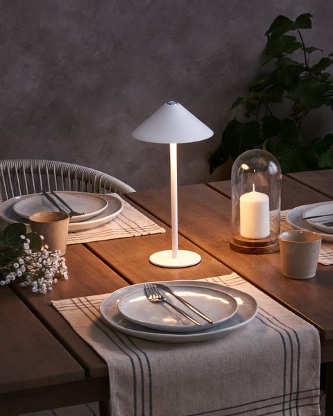 Tischdekoration mit Lampe, Tellern, Besteck und Kerze unter Glasglocke auf einem Holztisch