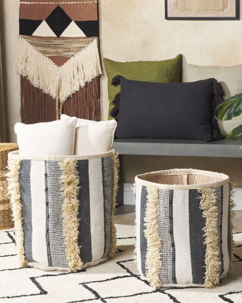 Dekorative Aufbewahrungskörbe mit Fransen auf einem gemusterten Teppich in einem Wohnzimmer.