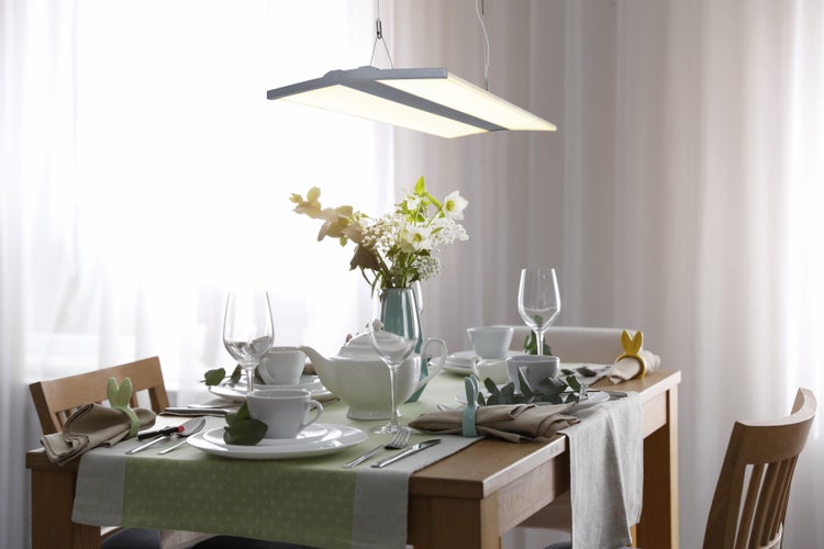 Gedeckter Esstisch mit Geschirr, Blumenvase und Hängelampe