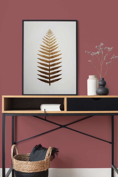 Moderner Holzschreibtisch mit schwarzer Schublade, darauf ein gerahmtes Bild mit goldenem Farnblatt, ein Buch und zwei dekorative Vasen.