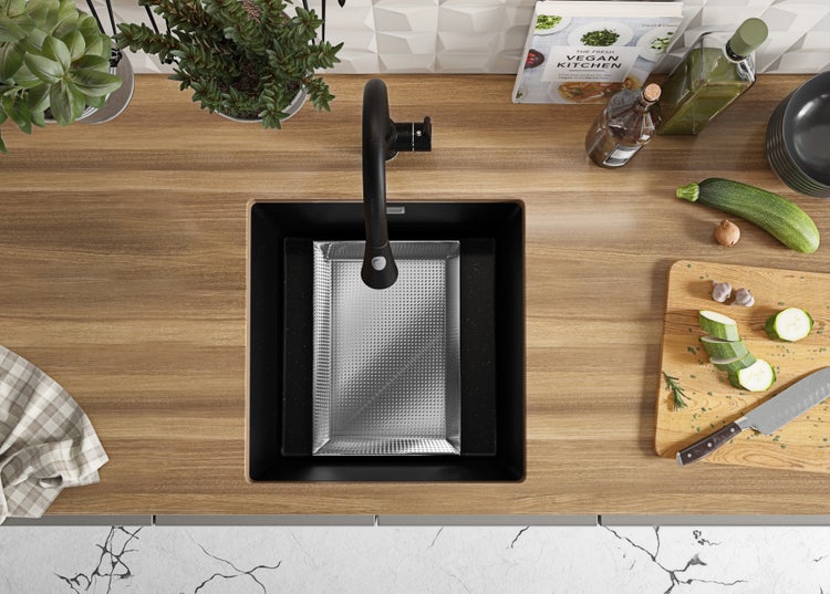 Spüle mit Abtropfschale, Armatur, Schneidebrett mit Zucchini, Kochbuch und Kräutern auf einer Küchentheke