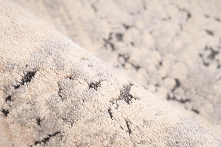 Nahaufnahme eines Teppichs mit hohem Flor und abstraktem Marmormuster in Creme und Grau.