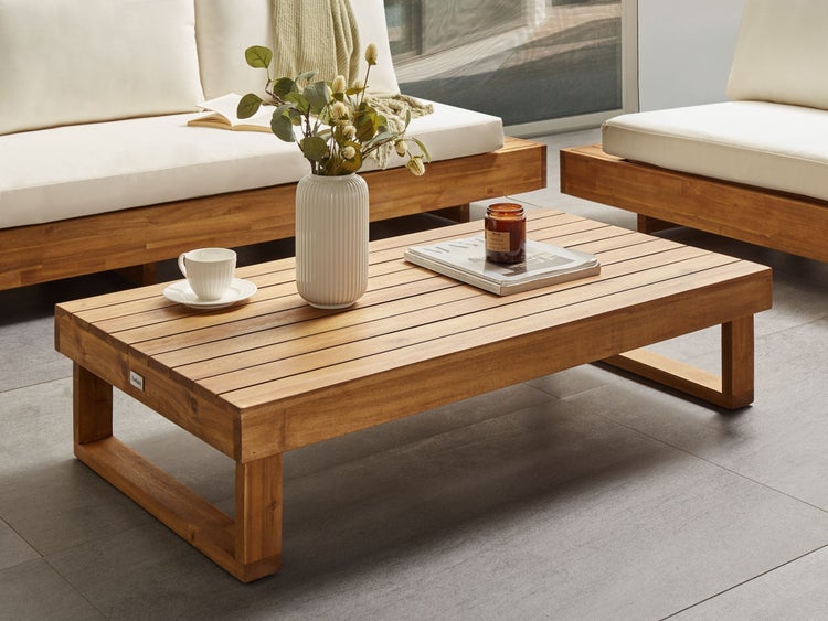 Gartentisch aus Holz mit Dekoration und Gartenmöbeln im Hintergrund