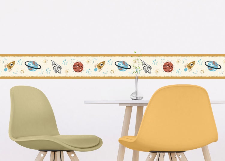 Tapetenbordüre für Kinderzimmer mit Weltraum-Motiven wie Planeten, Raketen und Sternen an einer Wand über einem Tisch in einem hellen Raum.