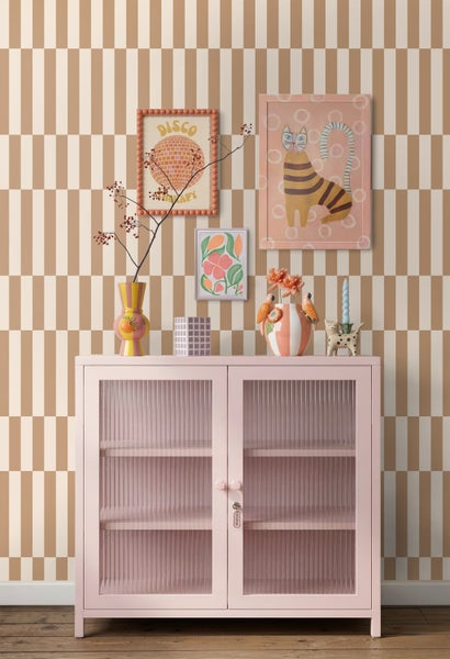 Vliestapete mit geometrischem Schachbrettmuster in Beige und Weiß hinter einem rosa Metallschrank mit Dekoration.