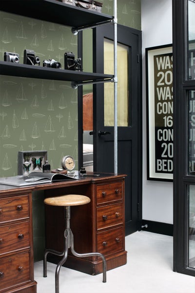 Vliestapete mit Segelschiff-Motiven in einem Arbeitszimmer mit antikem Holzschreibtisch, Metallhocker und schwarzen Industrieregalen.