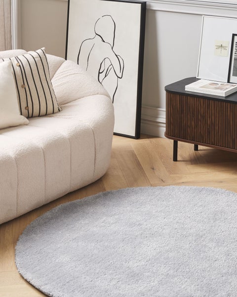 Wohnzimmerszene mit rundem Teppich, Sofa, Kunstwerken und Kommode für eine helle und organisierte Atmosphäre