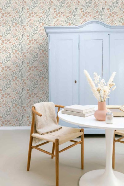 Hell eingerichteter Raum mit floral gemusterter Vliestapete, einem hellblauen Schrank, einem weißen Rundtisch und einem Holzstuhl.