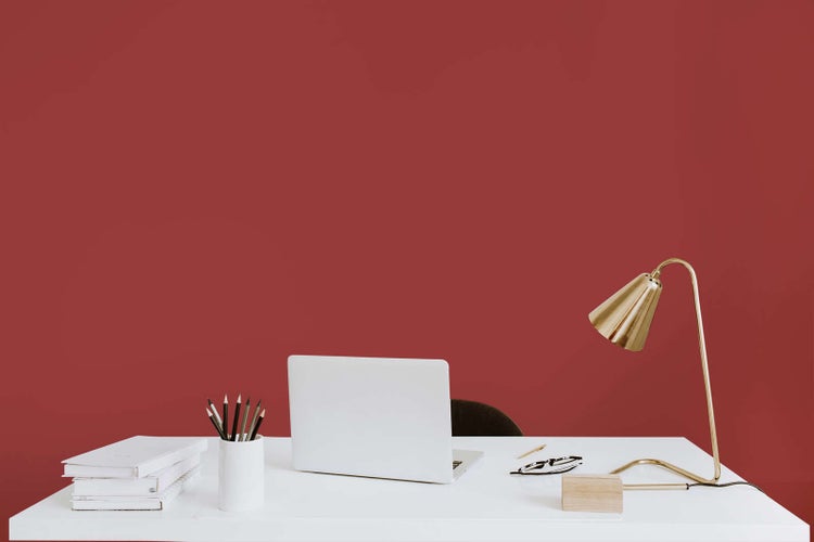 Moderner Arbeitsplatz mit weißem Schreibtisch, Laptop, goldfarbener Schreibtischlampe und Schreibutensilien.