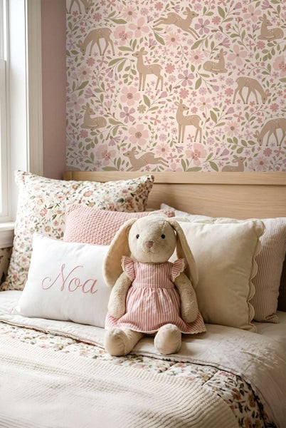 Kinderzimmer mit Tapete mit Rehmotiv und Blumenmuster, dazu ein Bett mit Kuscheltier und Zierkissen.