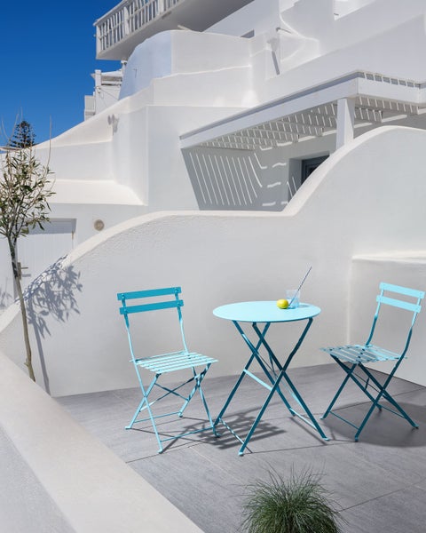 Terrassenszene mit blauem Gartentisch und zwei passenden Klappstühlen vor einem strahlend weißen Gebäude