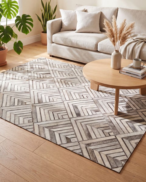 Wohnzimmer mit hellen Möbeln und einem rechteckigen Patchwork Teppich mit geometrischem Muster auf einem Holzboden.